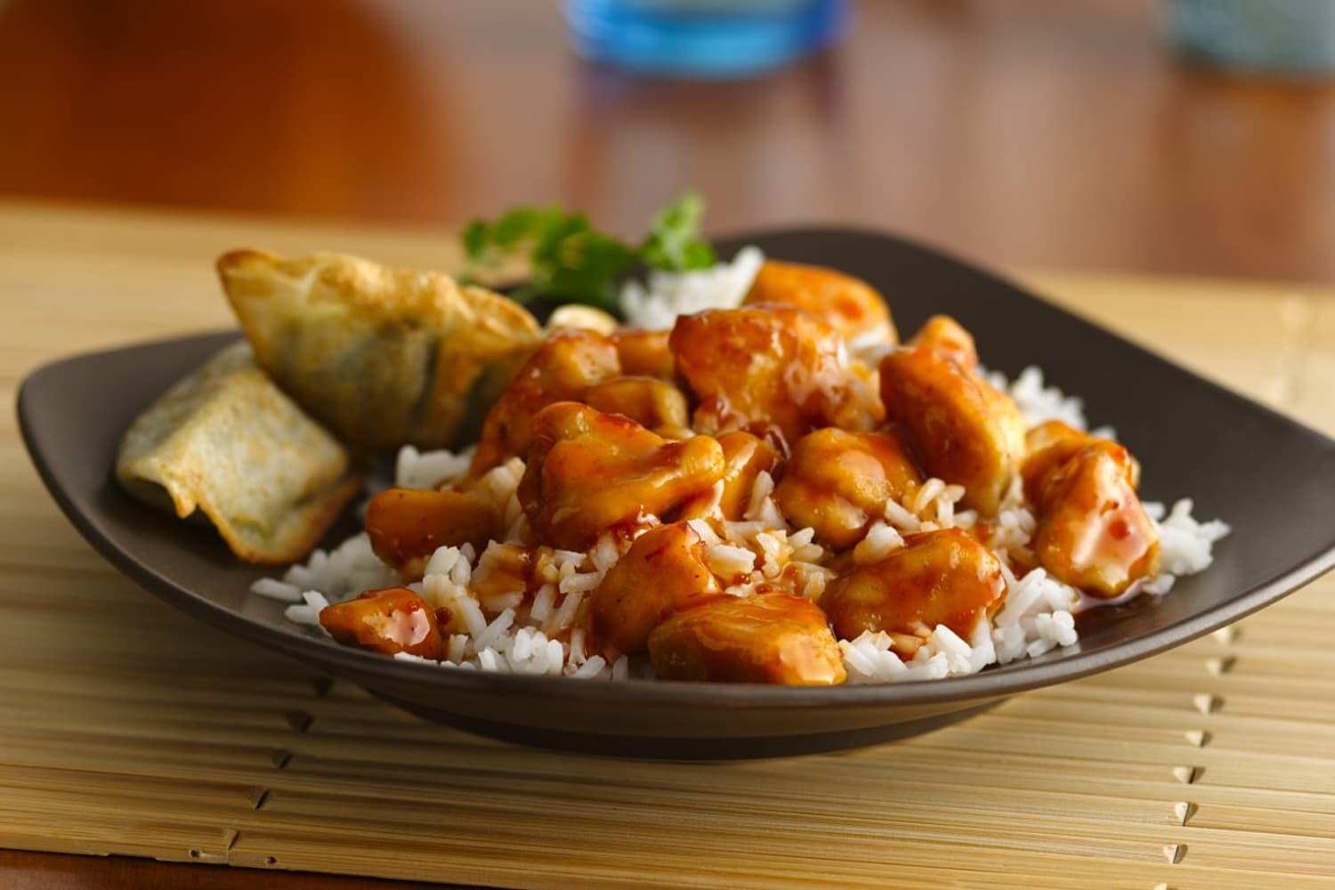 A square black plate with rice, dumplings and orange chicken